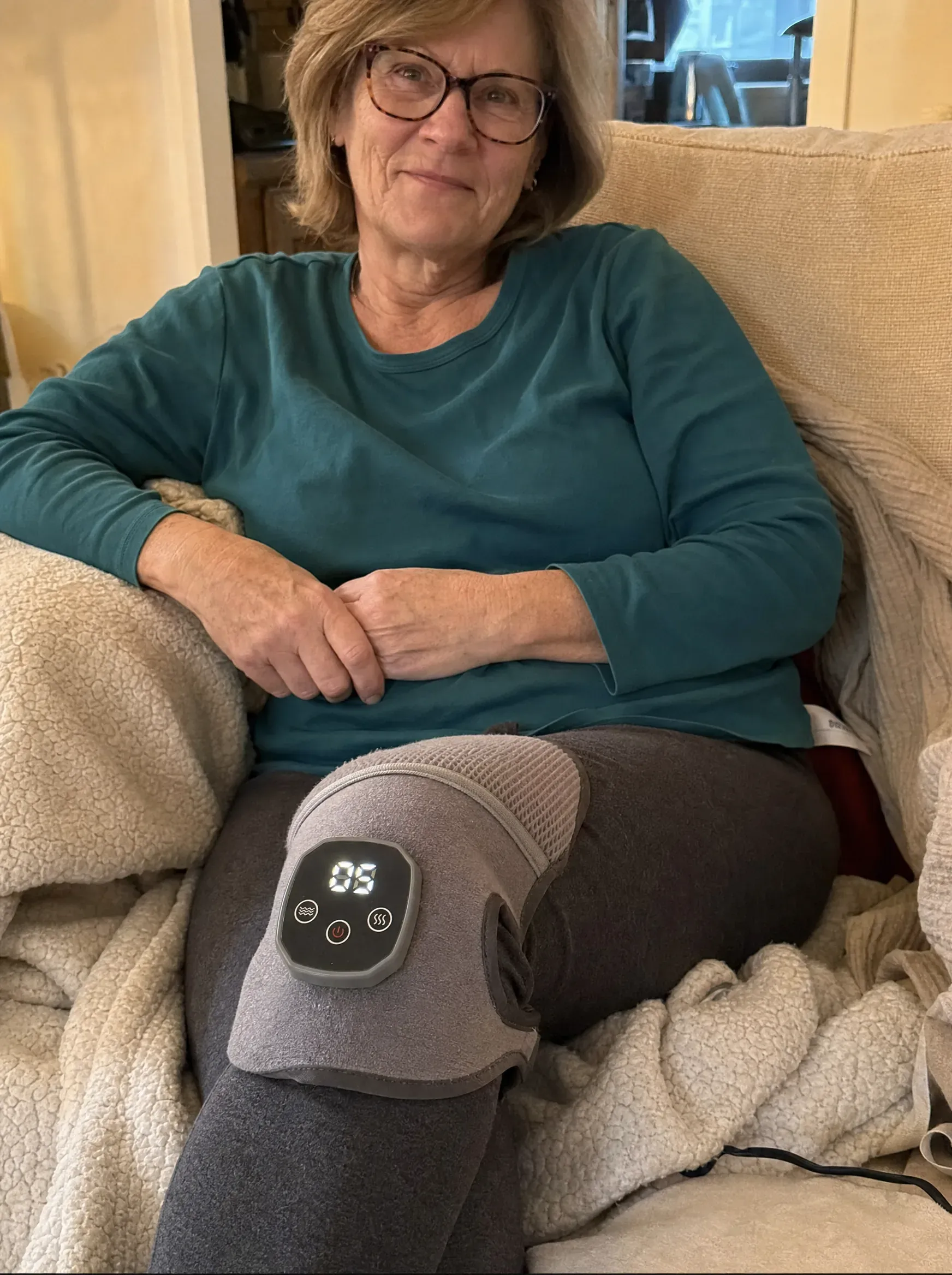 An older adult relaxing on the couch with the ReliefMD Knee Massager on the knee