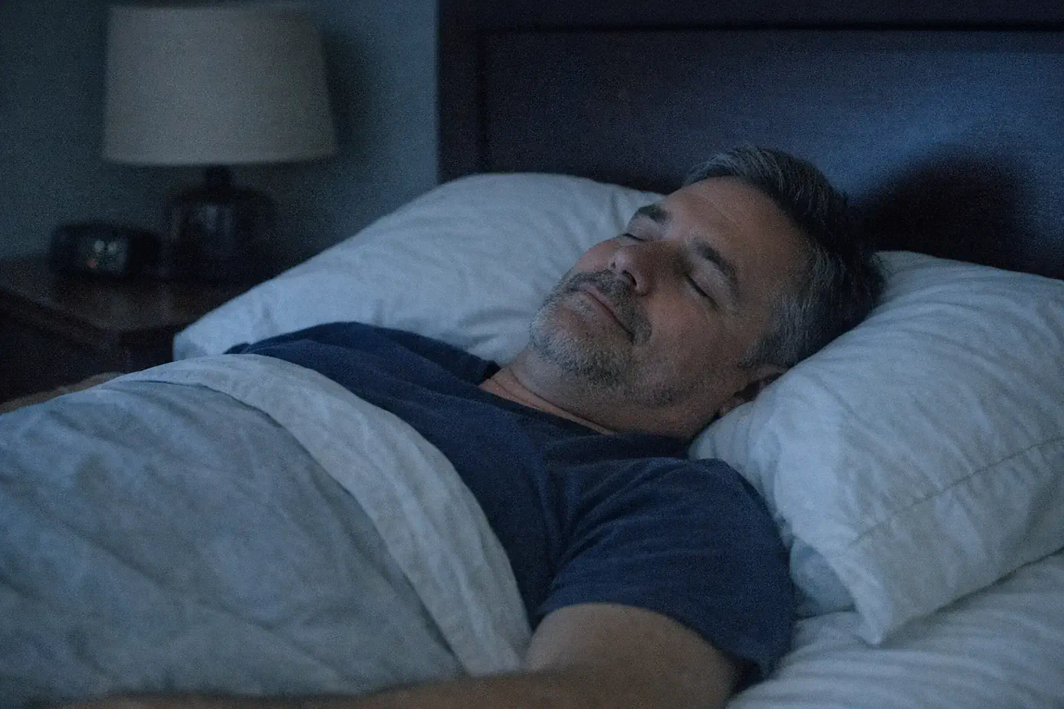 Bedroom lamp off, man sleeping flat on back peacefully